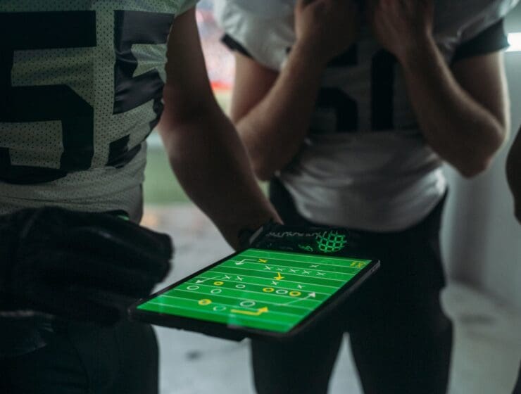 Medium stock shot of football players huddled around an iPad looking at plays via Xs and Os.